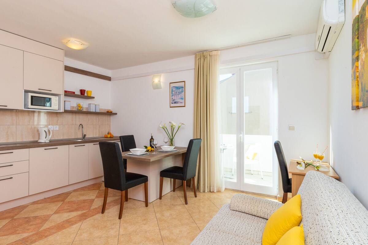 A compact living space with a kitchenette, dining area, and a sofa with yellow cushions.