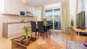A modern kitchen with a dining area, a flat-screen TV, and a balcony with a view of the hills. - Villa Erna (Dubrovnik)