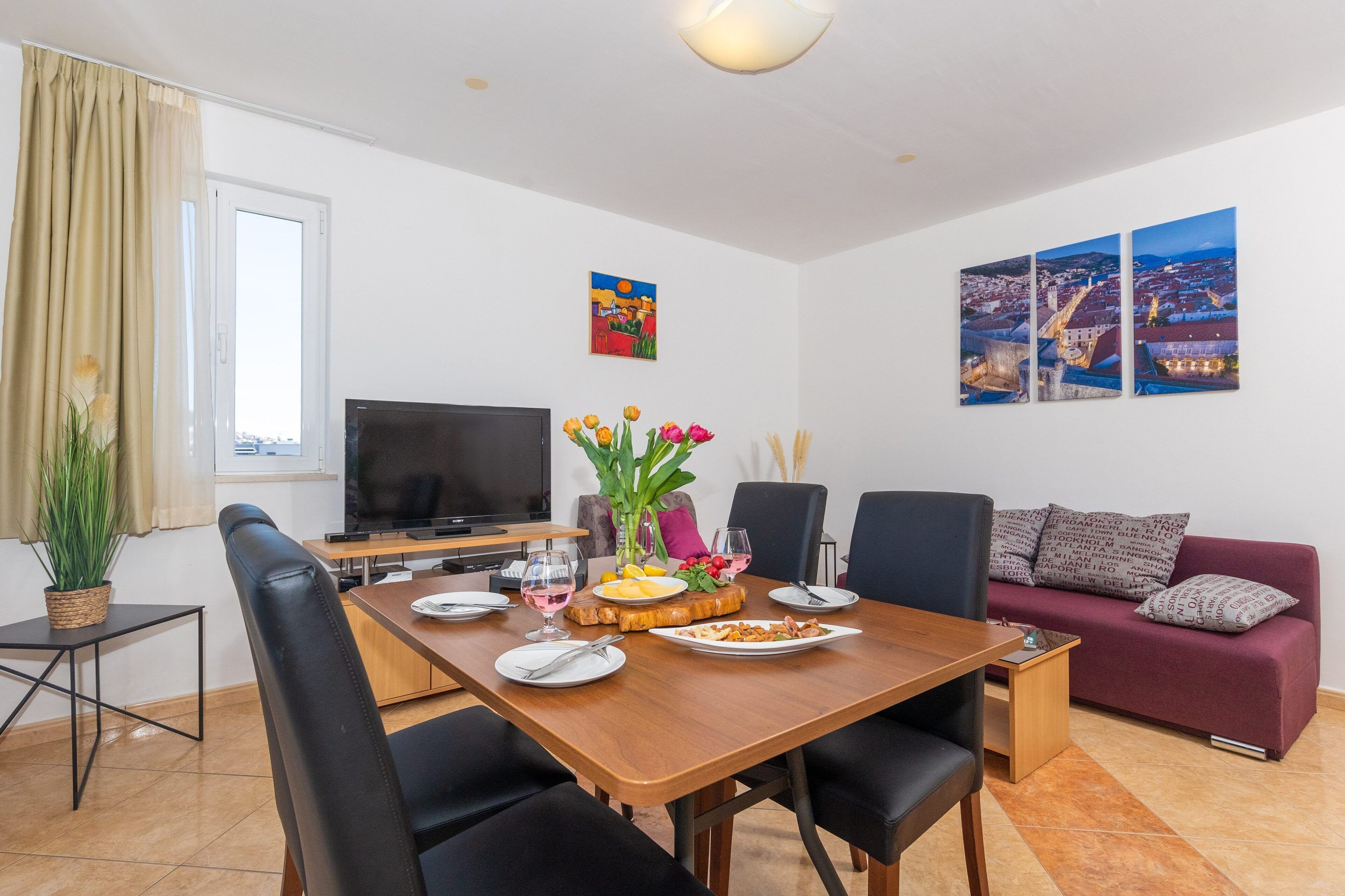 Ein Essbereich mit einem Holztisch, schwarzen Stühlen, einem Fernseher und einer Couch.