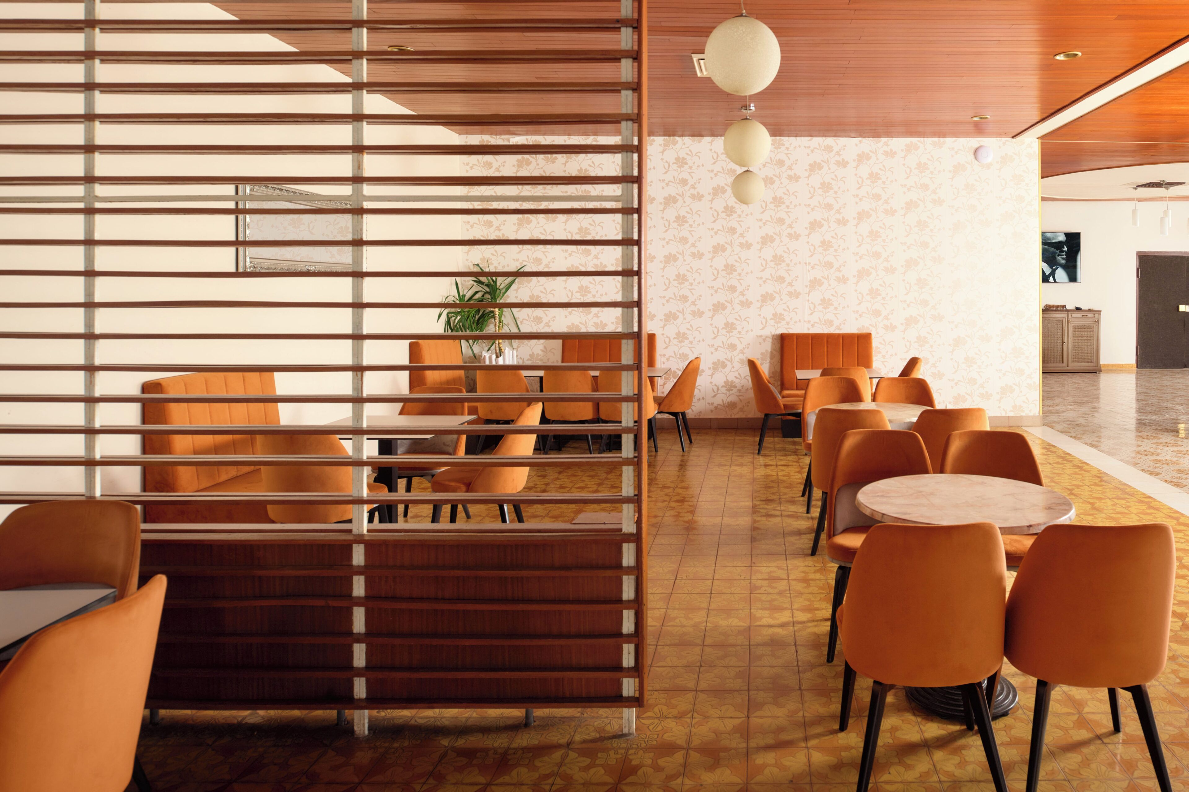A modern dining area with orange chairs and tables, a wooden partition, and a decorative plant.
