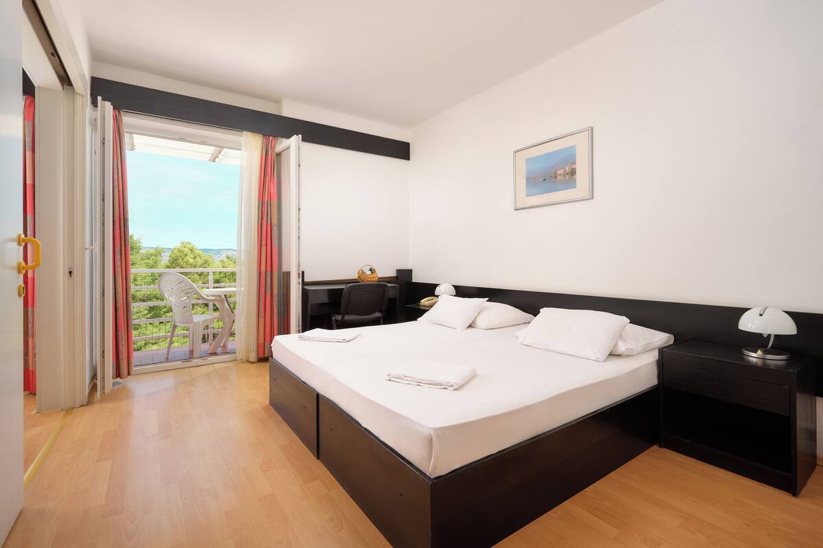 A bedroom with a bed, bedside table, chair, desk, and a view through a sliding door.