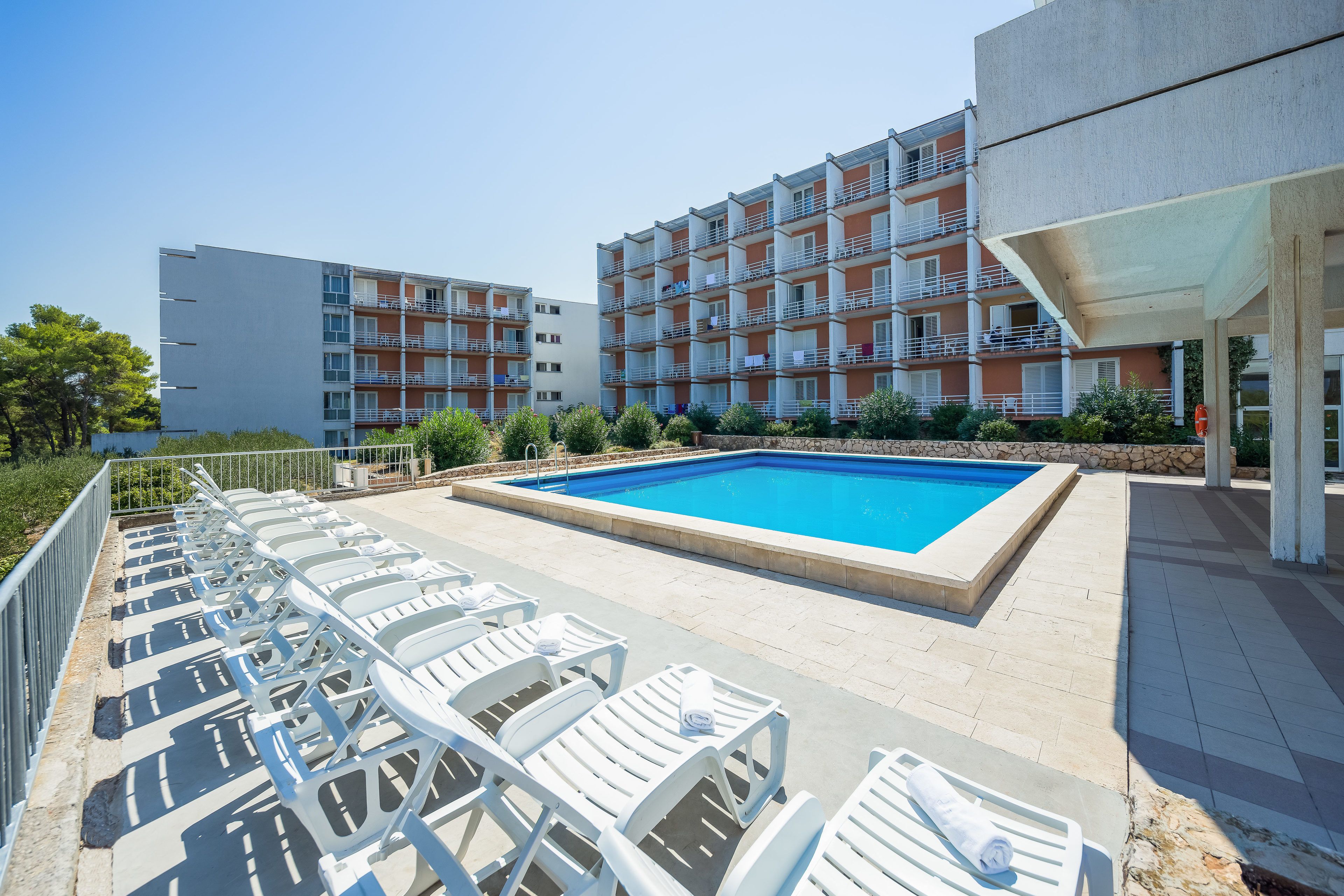 A swimming pool with lounge chairs and a building with balconies in the background.