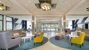 Un vestíbulo amplio con mobiliario moderno, una lámpara central y entrada de cristal.