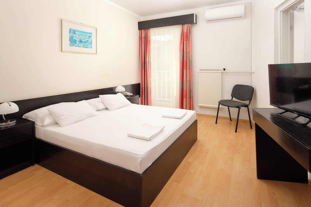 Une chambre d’hôtel avec un lit, un bureau avec une télévision, une chaise et un tableau au mur.