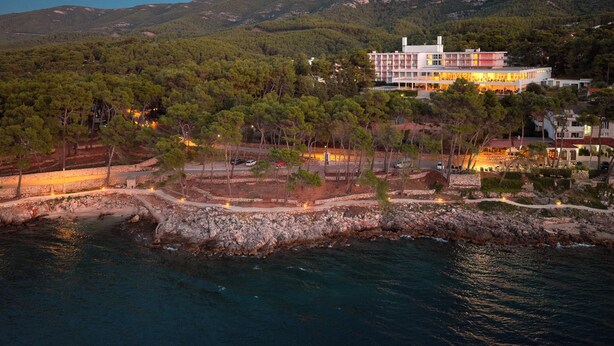 A coastal hotel with a large building, a rocky shoreline, and a forested hillside.