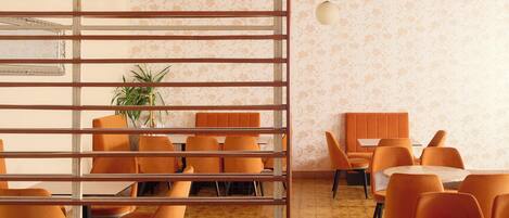 Un comedor moderno con sillas y mesas anaranjadas, un separador de madera y un muro con diseño.