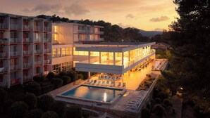 A modern hotel with a pool, multiple balconies, and a well-maintained garden.