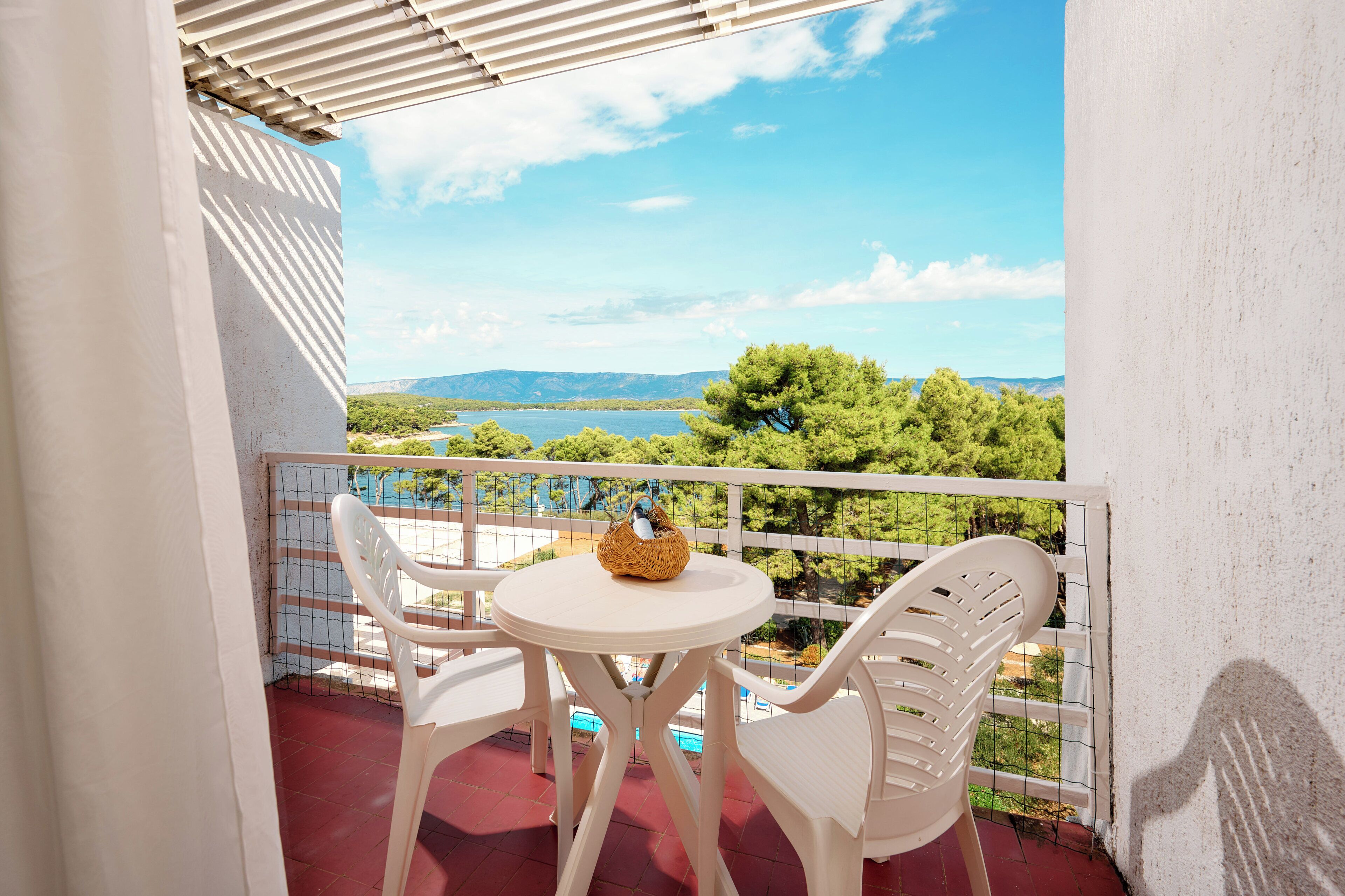 Varanda com uma mesa branca e duas cadeiras de plástico branco, com vista para um lago e montanhas.