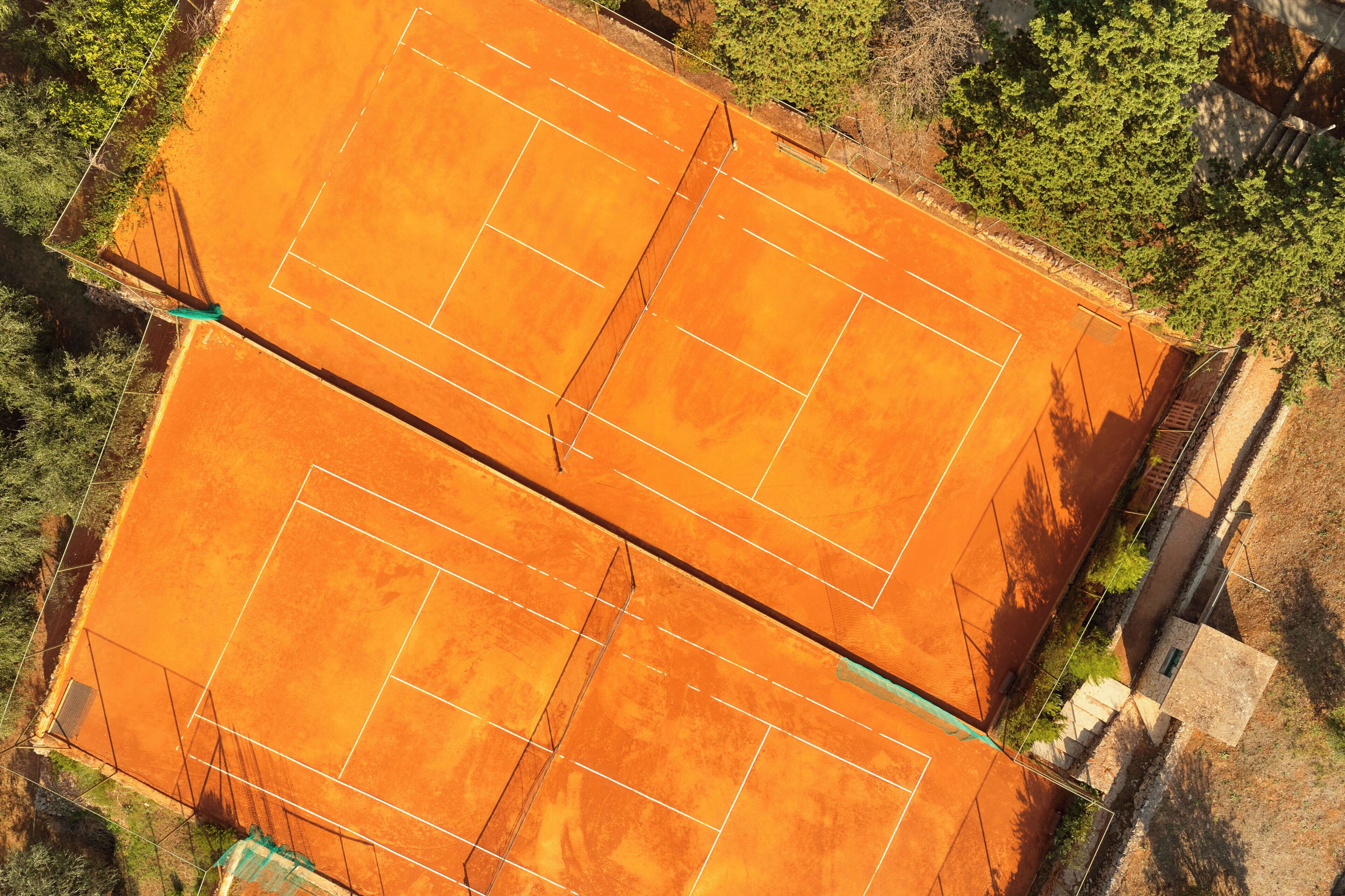 A tennis court with a net, surrounded by trees and a fence.