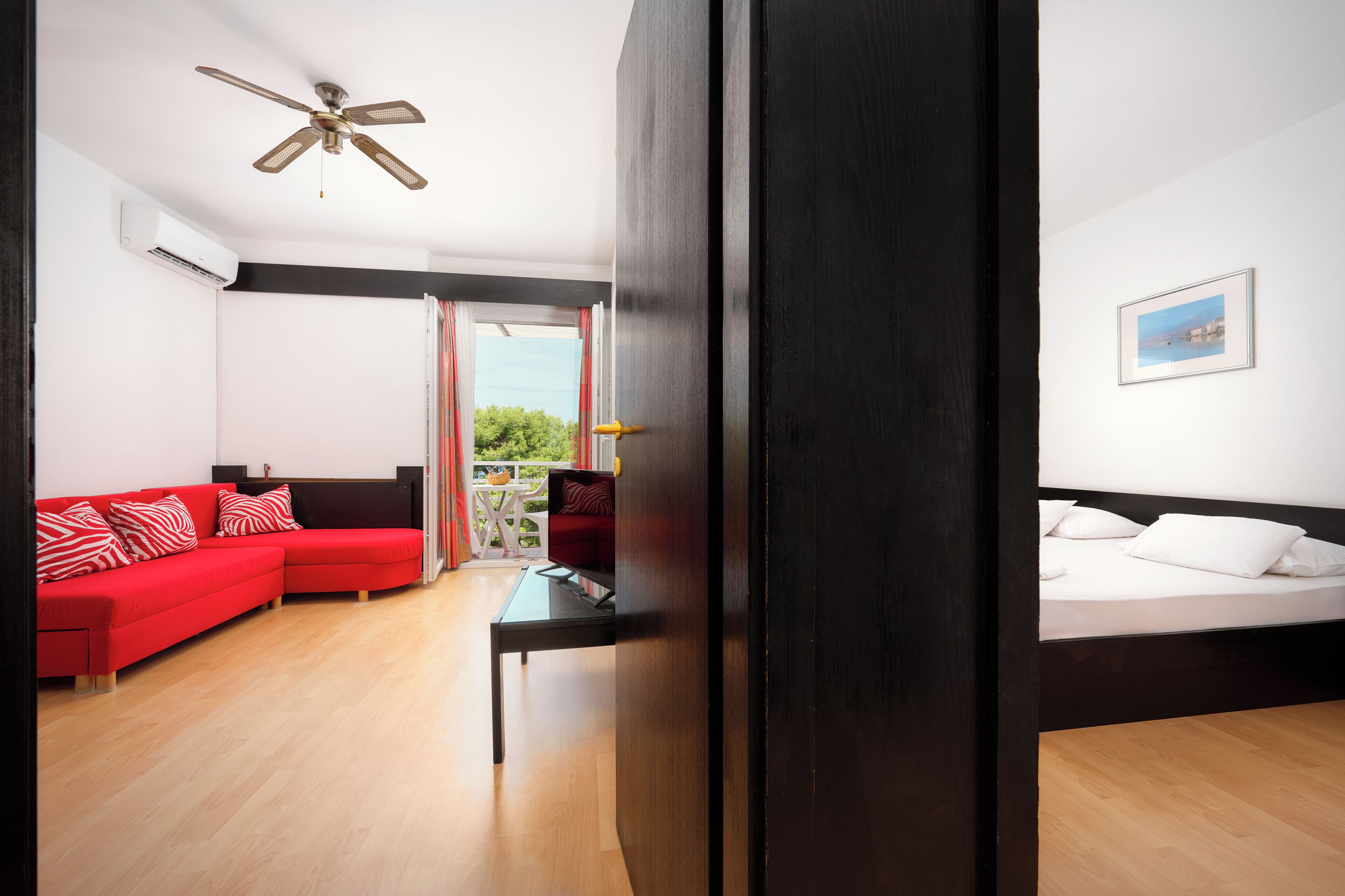 A modern hotel room with a red sofa, a white bed, and a ceiling fan.