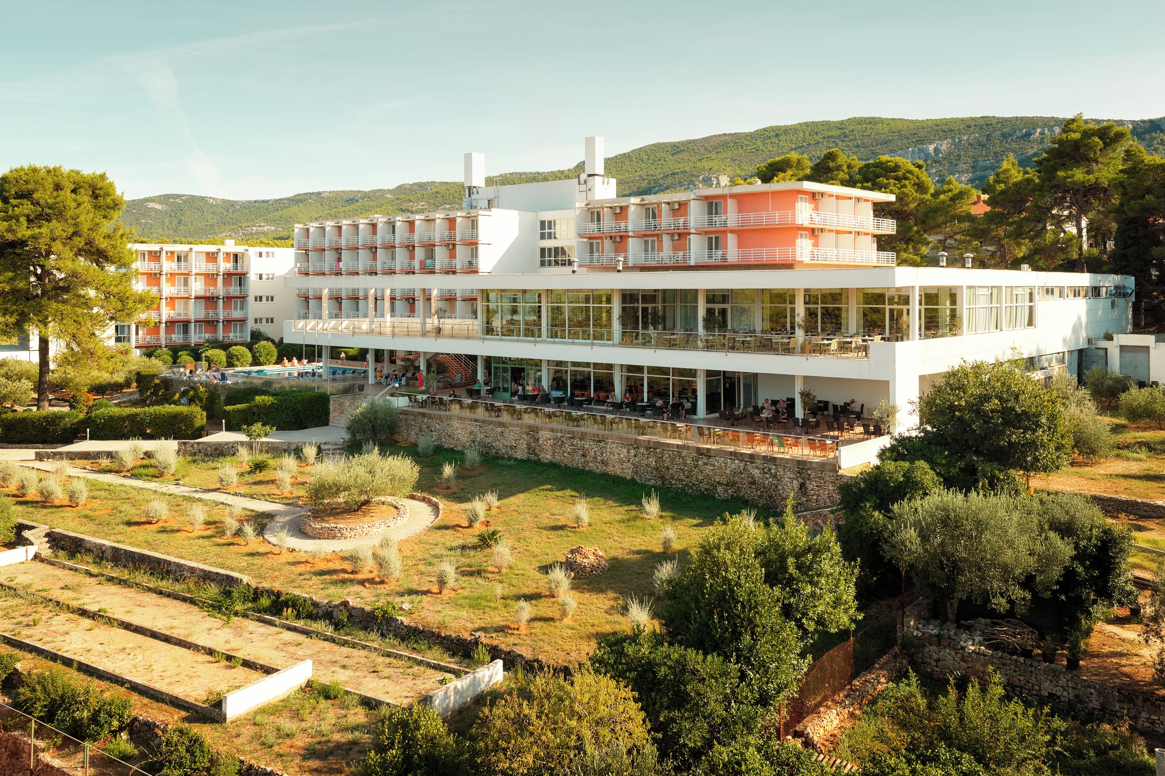 A modern hotel with multiple floors, outdoor seating areas, and a landscaped garden.
