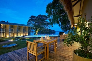 A wooden deck with a table and chairs, a pool, and a building with large windows. - Ekho Safari Tissa Hotel (Thissamaharama)