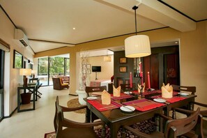 A dining area with a table set for four, chairs, a hanging light fixture, and a view of the outdoors through large windows. - Ekho Safari Tissa Hotel (Thissamaharama)