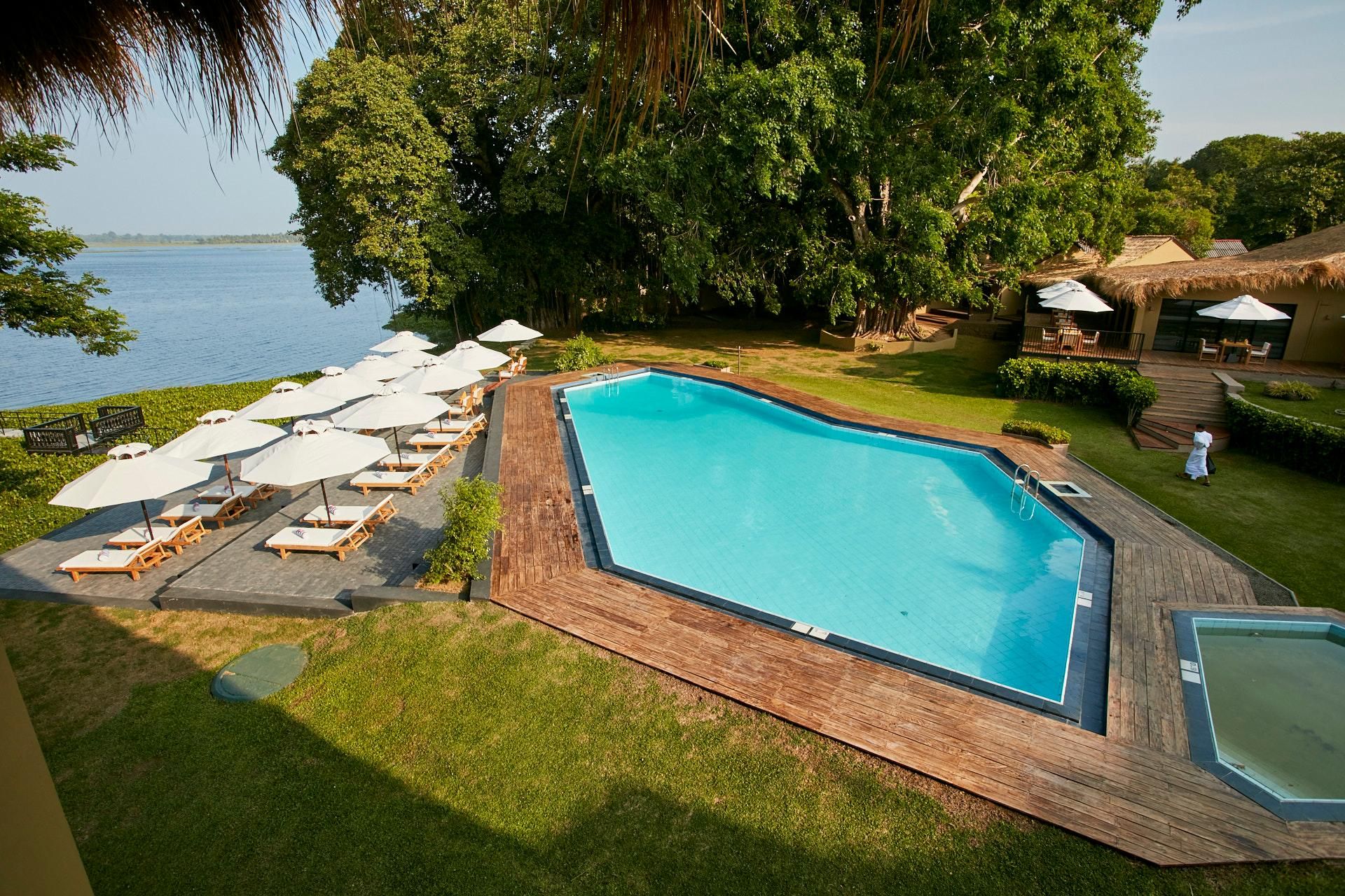 A swimming pool with lounge chairs and umbrellas, surrounded by greenery and a view of the water.