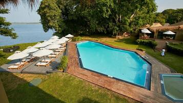 A swimming pool with lounge chairs and umbrellas, surrounded by greenery and a view of the water.