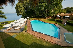 Piscina com espreguiçadeiras e guarda-sóis, cercada por vegetação e vista para a água.