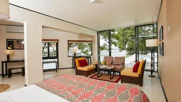 A modern hotel room with a large bed, two sofas, a desk, and a view of the outdoors.