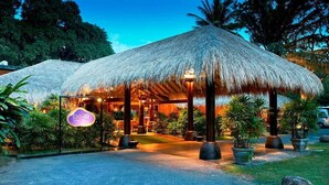 A resort with thatched-roof structures, a signboard, and potted plants.