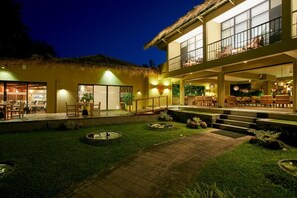 Um hotel com telhado de palha, área de estar externa e um pátio bem iluminado.