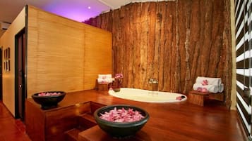 A spa room with a wooden wall, a bathtub, a wooden bench, and a bowl of pink flowers.