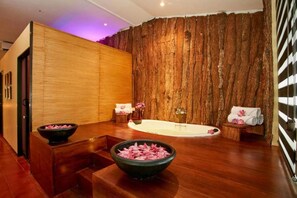 A spa room with a wooden wall, a bathtub, a wooden bench, and a bowl of pink flowers. - Ekho Safari Tissa Hotel (Thissamaharama)