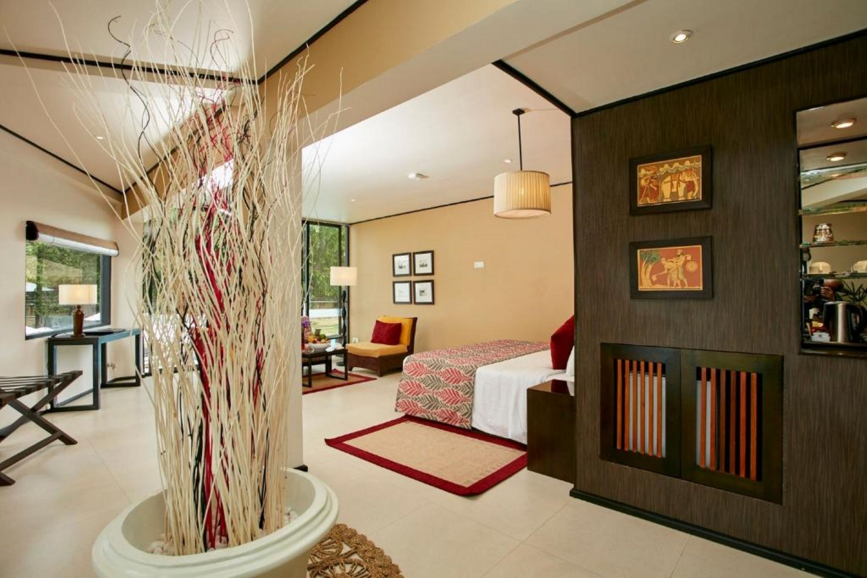 Une chambre d’hôtel moderne dotée d’une grande fenêtre, d’un lit recouvert d’une couvre-lit à motifs rouges et blancs, d’un coin salon avec un fauteuil et une table, et d’un panneau décoratif mural.
