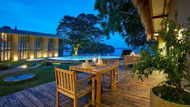A wooden deck with a table and chairs, a pool, and a building with large windows.