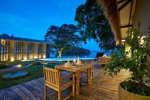 A wooden deck with a table and chairs, a pool, and a building with large windows.