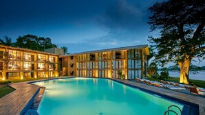 A modern hotel with a swimming pool, multiple balconies, and a view of a lake.