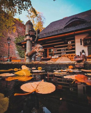A rustic building with a pond, autumn leaves, and a wooden structure. - Romantik Hotel U raka (Prague)