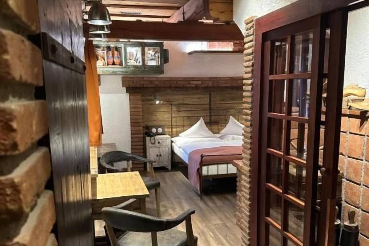 A cozy room with a bed, a table, and chairs, wooden walls, and a brick wall.