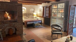 Une pièce chaleureuse avec une cheminée, un lit, une table à manger et un buffet aux portes vitrées.