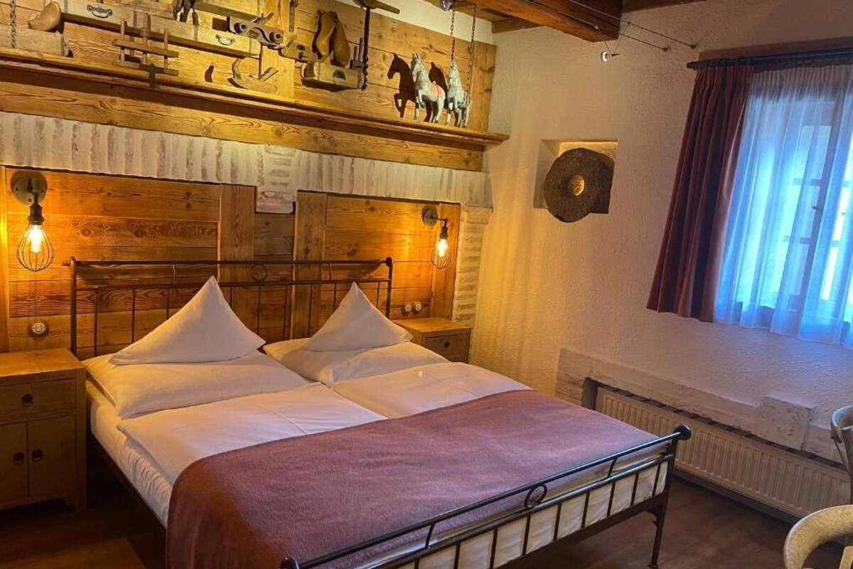 A bed with a headboard, bedside lamps, a window with curtains, and wooden wall decor.