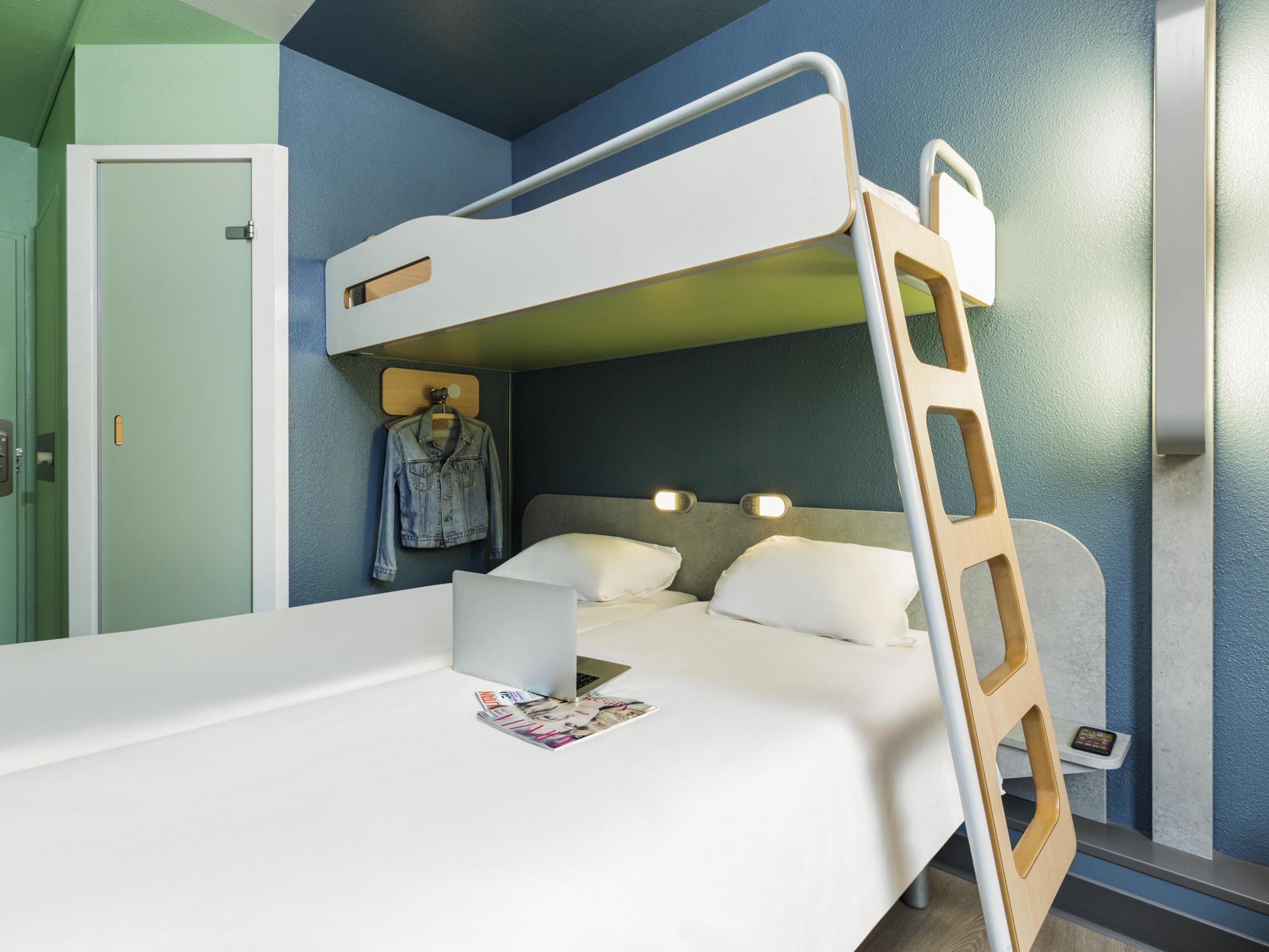 A bunk bed with a ladder, a desk with a laptop, and a hanging jacket.