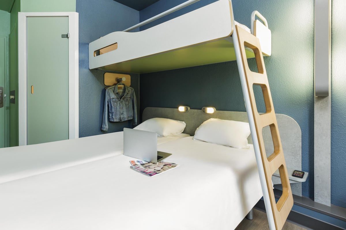 A bunk bed with a ladder, a desk with a laptop, and a hanging jacket.