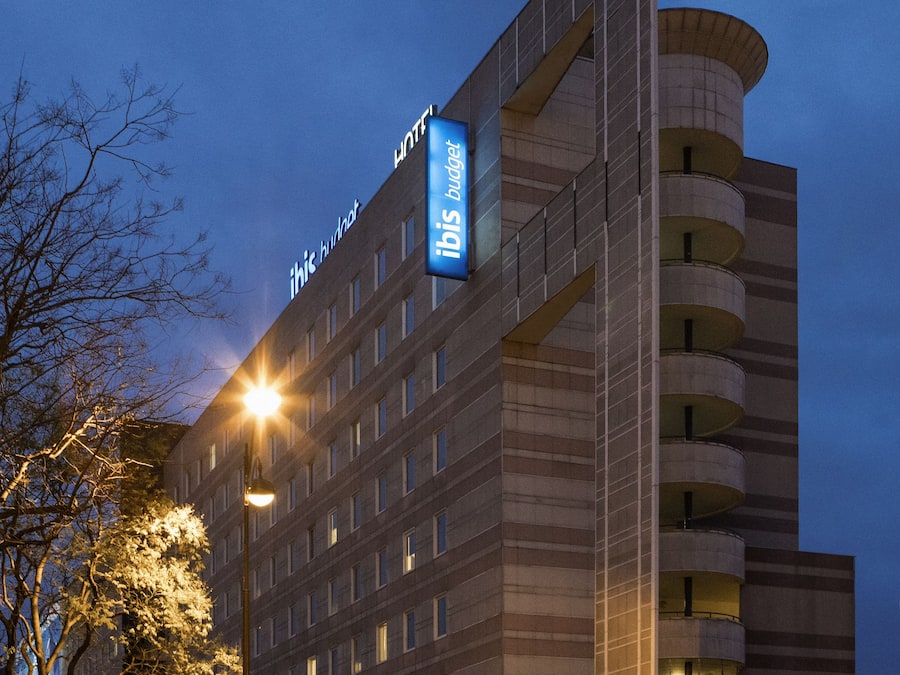 Hotel com placa chamativa, vários andares e área de estacionamento.