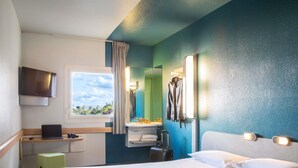 Habitación de hotel con cama, escritorio con computadora portátil, ventana con vista, lavamanos y espejo.