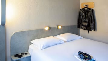 Une chambre d’hôtel avec un lit, une table de chevet et une veste en cuir accrochée au mur.