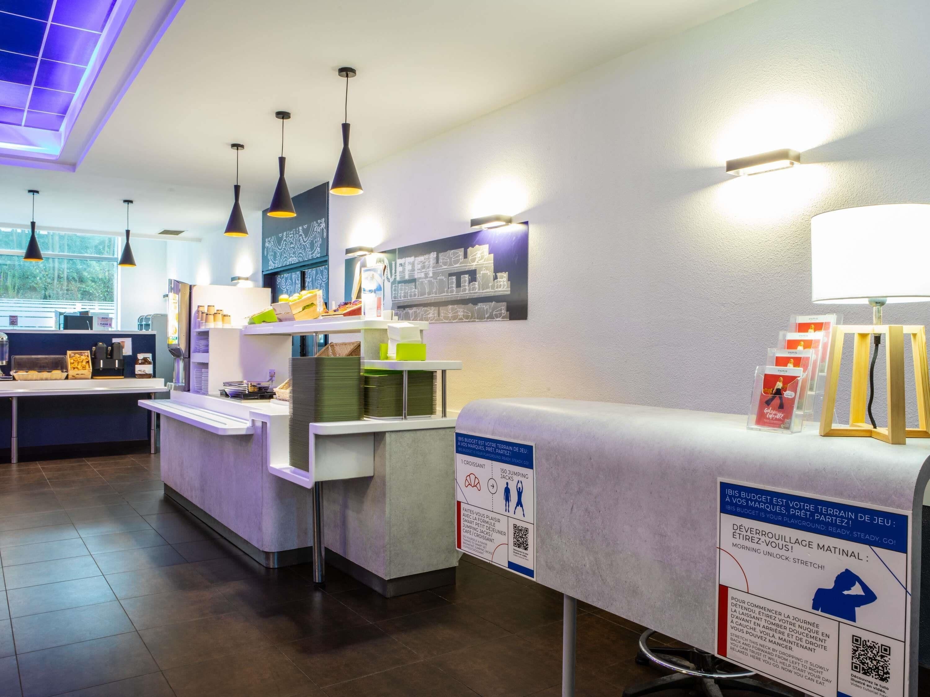 A modern indoor space with a reception desk, multiple pendant lights, and informational posters on the walls.