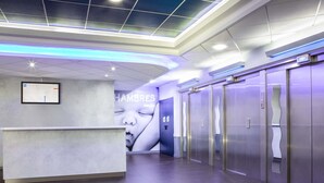 Un área de recepción moderna con un mostrador, un anuncio grande en la pared y una fila de ascensores.