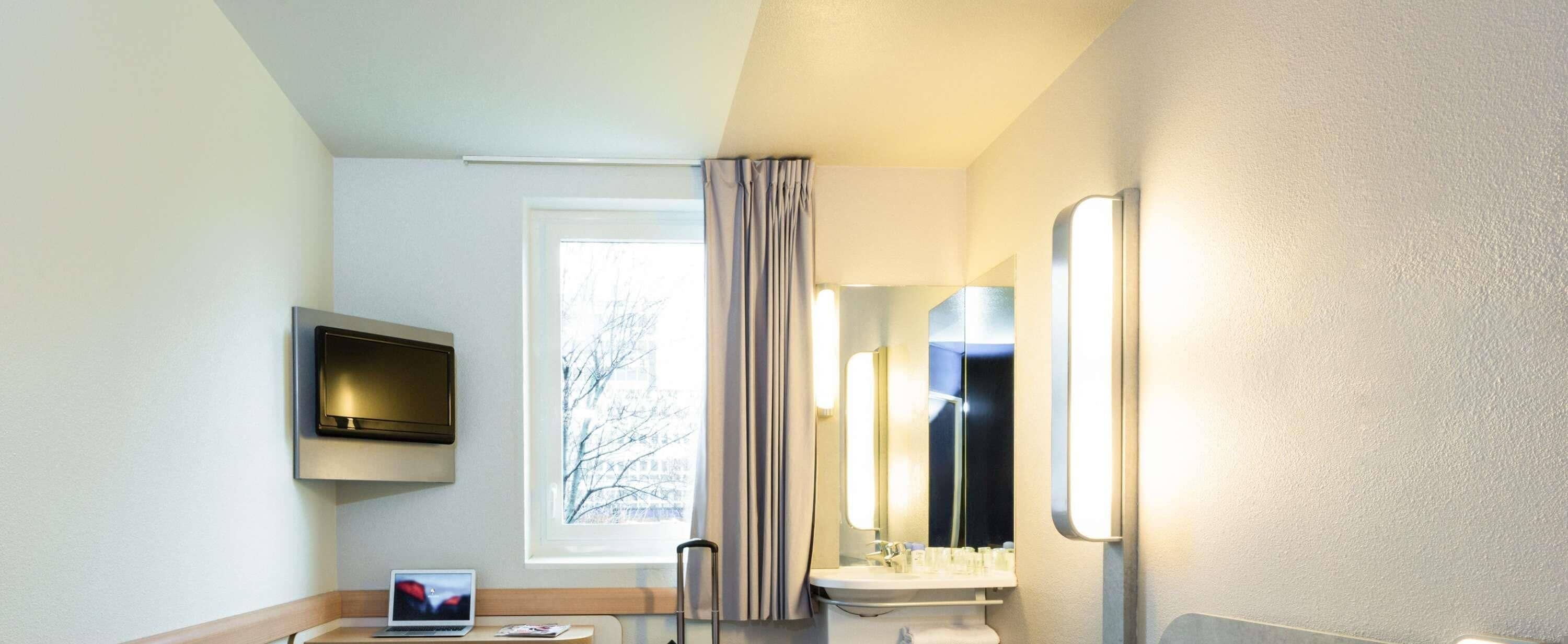 A hotel bathroom with a toilet, sink, mirror, and a TV mounted on the wall.