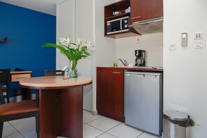 Et lille køkken med mikroovn, kaffemaskine og opvaskemaskine. Der er et spisebord med stole og en vase med blomster.
