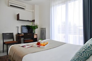 Une chambre d’hôtel avec un lit, un bureau avec un ordinateur, une chaise, une télévision et une fenêtre avec des rideaux.