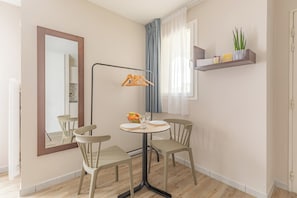 Un coin repas minimaliste avec une table ronde, quatre chaises, un miroir, une lampe sur pied et une étagère ornée d’une plante.