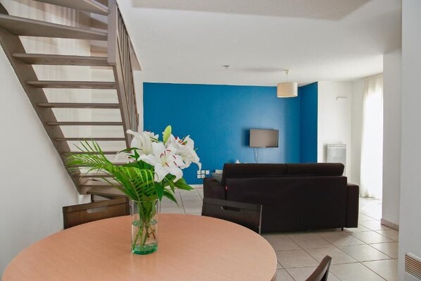 Een moderne woonkamer met een blauwe accentmuur, een zwarte bank, een televisie en een trap.