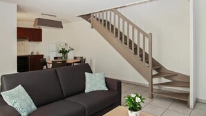 A modern living room with a sofa, a staircase, and a dining area in the background. - Park & Suites Toulouse Colomiers (Toulouse)
