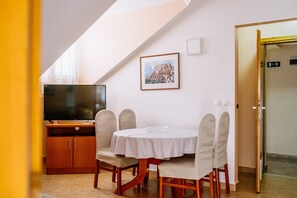 Uma sala de jantar com uma mesa, cadeiras, uma televisão e um quadro na parede.
