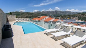 Una piscina en la azotea con sillas de descanso, vistas despejadas al mar y montañas al fondo.
