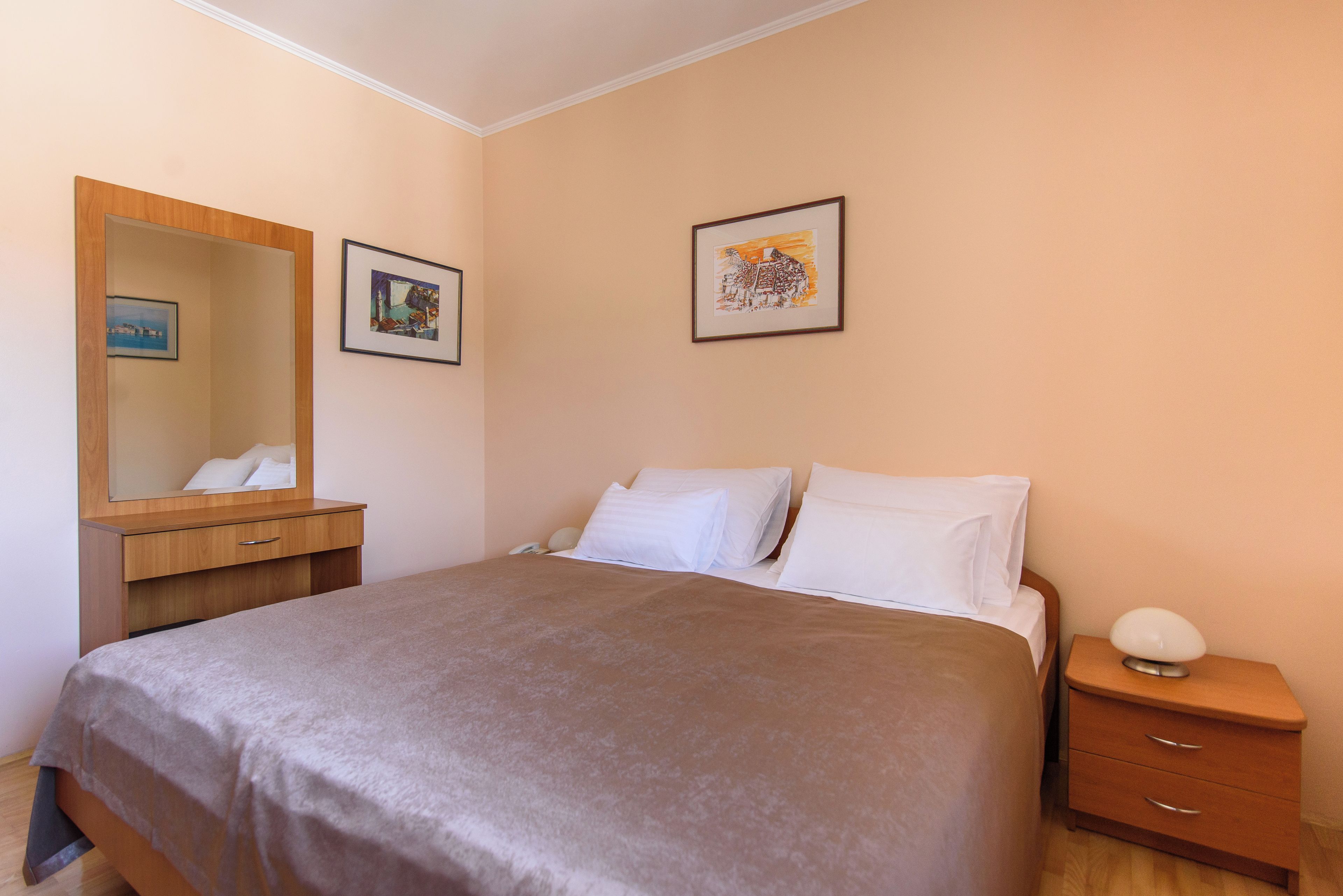 A hotel room with a bed, a bedside table, a nightstand, a mirror, and two framed pictures on the wall.