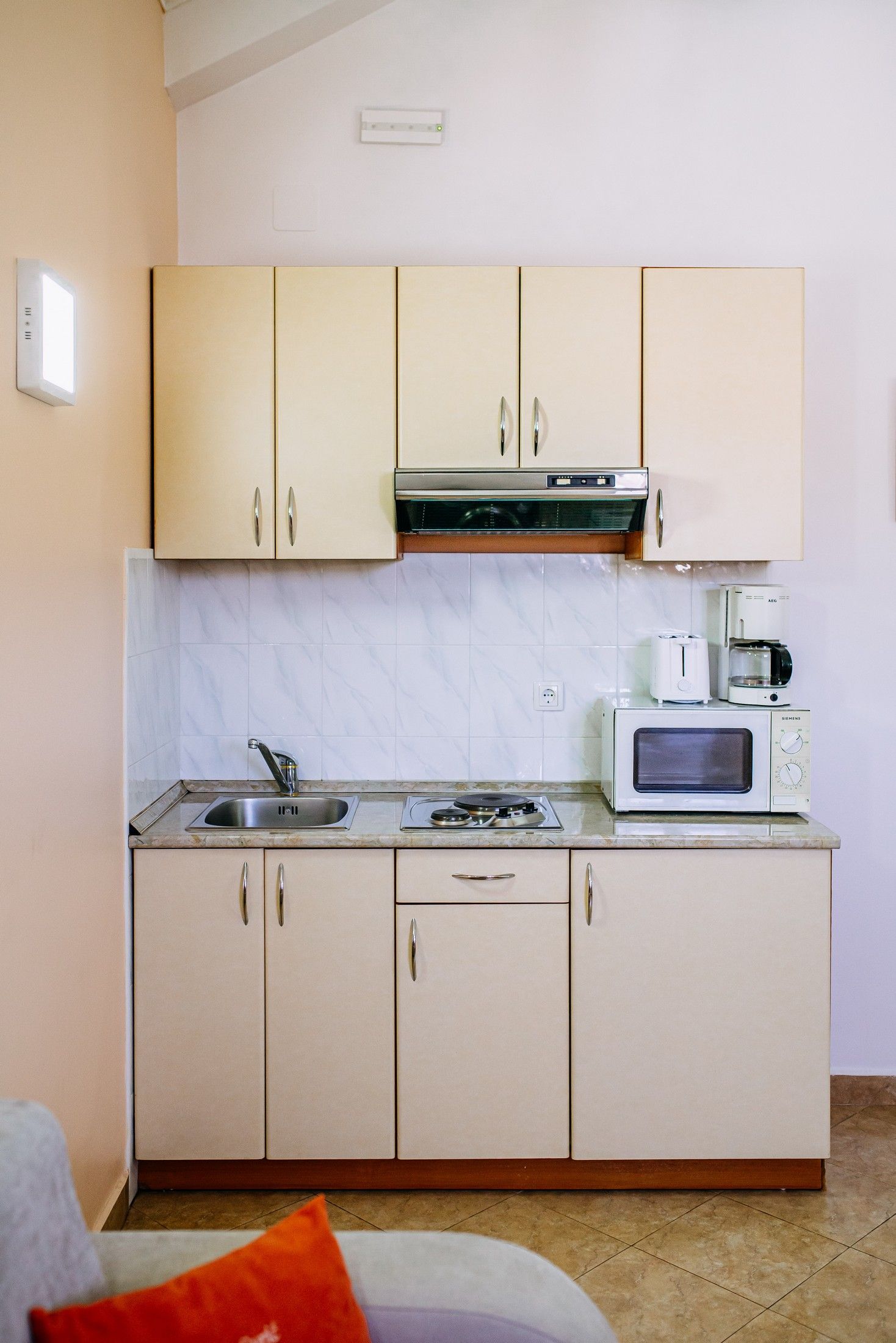 A compact kitchen with a microwave, toaster, and coffee maker on the countertop, a sink, and cabinets with handles.